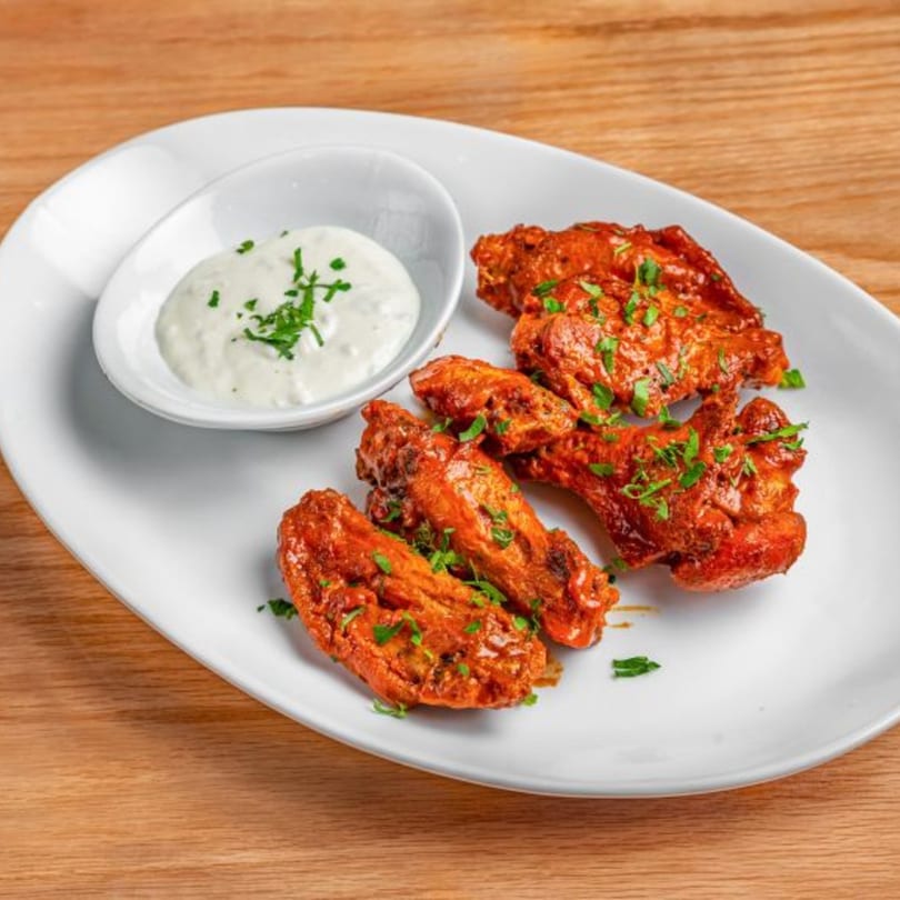 Spicy chicken wings with ranch dressing on a white oval plate, on a wooden table.