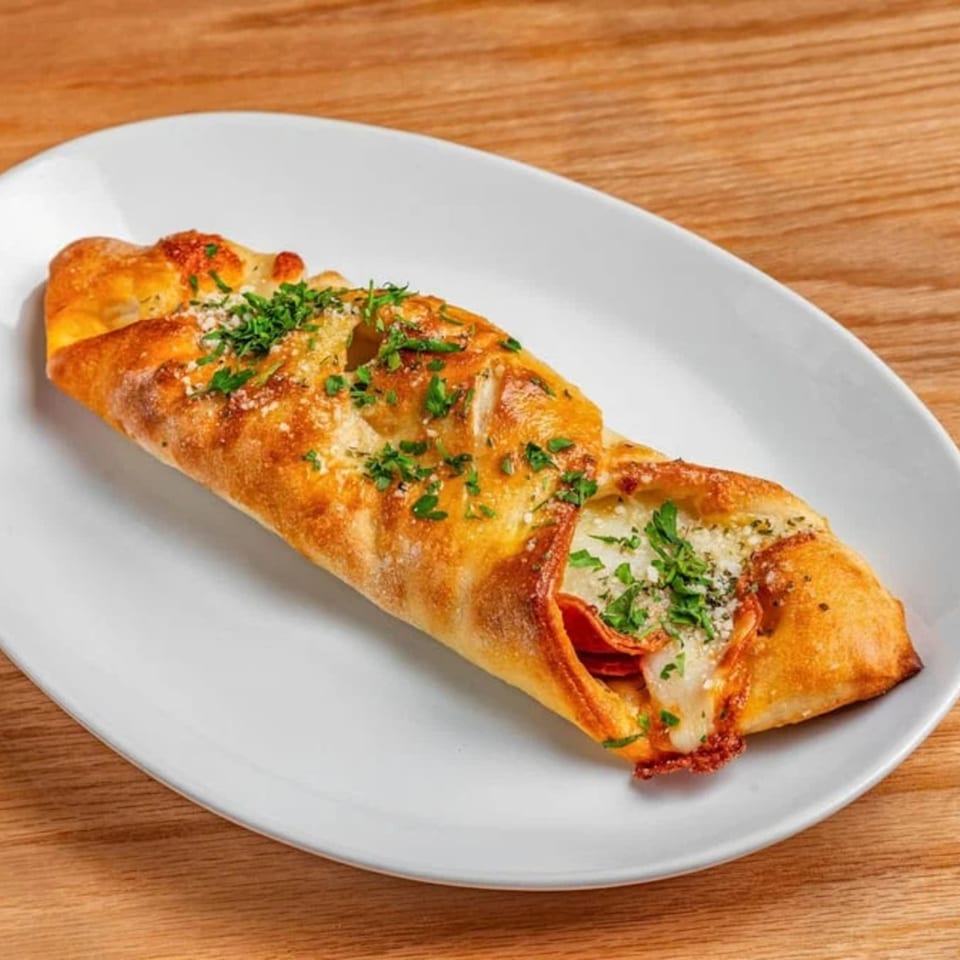 Golden-brown calzone, garnished with parsley and parmesan, on a white oval plate.