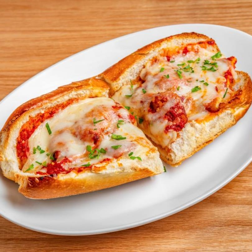 Two halves of a meatball sub sandwich with melted cheese and parsley on a white plate.