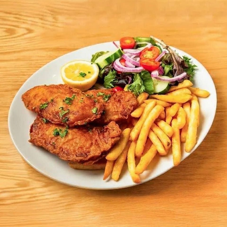 Golden-brown fried fish fillets with french fries, a side salad, and a lemon wedge on a white plate.